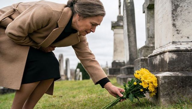 Senior woman placing yellow flowers at grave in cemetery, mourning and remembrance moment