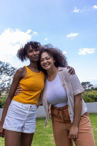 Smiling diverse female friends embracing on sunny lawn enjoying summer together