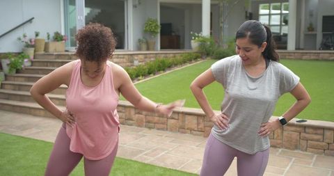 Diverse female friends stretching on home lawn near patio for backyard fitness workout