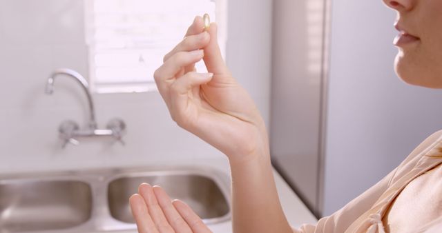 Woman holding a vitamin pill near kitchen sink in morning light. Perfect for health and wellness blogs, product promotions, daily routine illustrations, or dietary supplement advertisements.