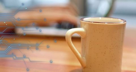 Speckled ceramic mug sitting on wooden desk with blue circuit overlay and blurred laptop
