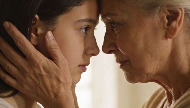 Senior woman caressing teen girl, holding face in tender intergenerational moment