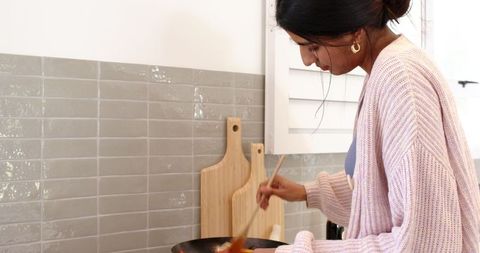 Woman cooking in modern kitchen stirring ingredients in pan
