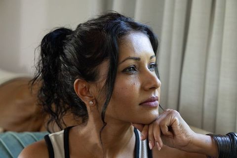 Pensive woman resting chin on hand gazing out window in cozy living room portrait