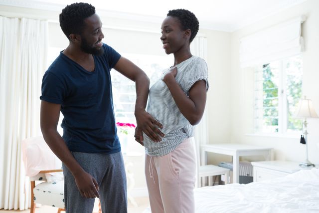 This image captures a joyful moment between a couple as they celebrate their pregnancy at home. The man is touching the woman's belly, symbolizing love and anticipation for their upcoming child. Ideal for use in articles or advertisements related to family, pregnancy, parenthood, and home life.
