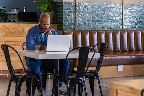Entrepreneur working remotely at coffeehouse laptop and takeaway cup in industrial café