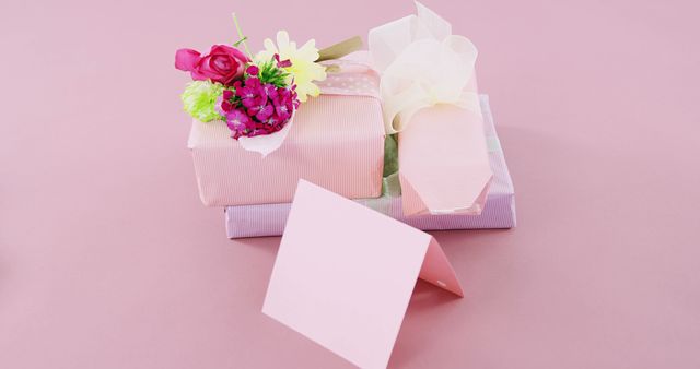 Gift boxes adorned with delicate flowers and a blank pink card rest on a pastel background, with copy space. Perfect for conveying messages of appreciation or celebration during special occasions like Mother's Day or birthdays.