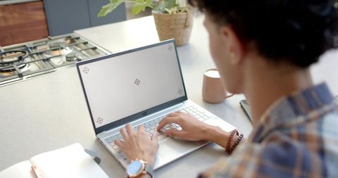 Man typing on laptop at kitchen counter for remote work with blank screen and daylight
