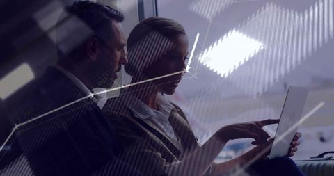 Executive duo collaborating on tablet through glass reflections in modern office lounge