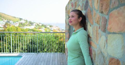 Woman leaning on stone wall by pool overlooking coastal ocean view, contemplative moment