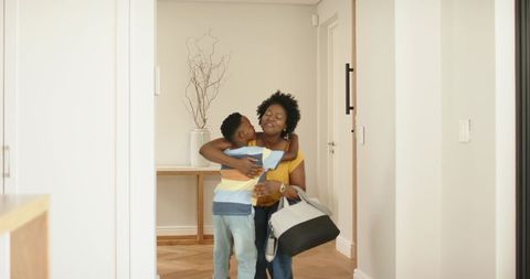 African american mother hugging school-age son in entryway carrying two-tone duffel bag