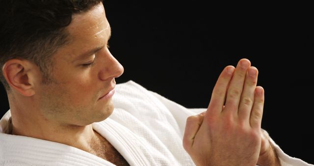 Martial artist in a white gi intensely concentrating while practicing a hand technique against a dark backdrop. Perfect for martial arts schools' websites, self-defense training materials, sports ads, discipline-oriented campaigns.