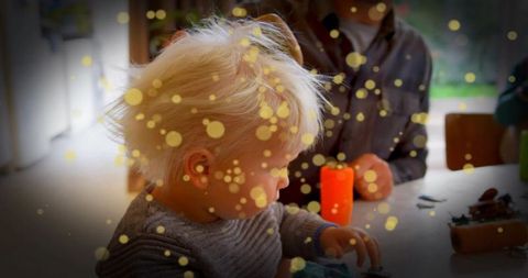 Toddler exploring crafts at kitchen table with warm led candlelight and grandparent nearby