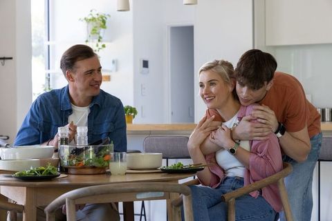 Modern family sharing relaxed meal in bright kitchen with hug and homemade salad