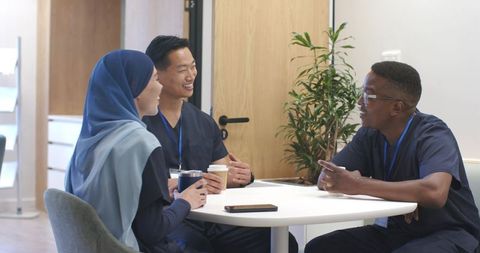 Multicultural healthcare team taking coffee break in clinic lounge, smiling staff chatting