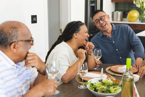Diverse friends laughing over white wine around dining table sharing salad and stories