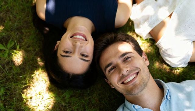 Young couple lying on grass smiling under dappled sunlight relaxed summer romance and friendship