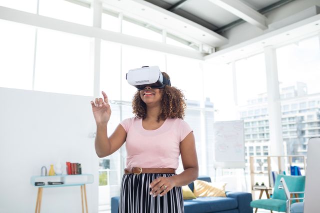 An African-American woman engages with a virtual reality headset in a bright, modern office space. This can be used to depict innovation, the future of work, and how technology enhances business environments. Suitable for websites, articles, or presentations focused on technology integration, workplace innovation, or virtual reality applications.