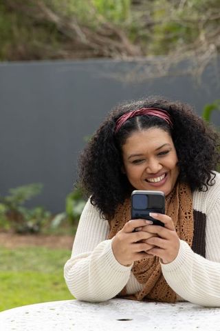 African american woman smiling while using smartphone at outdoor garden table