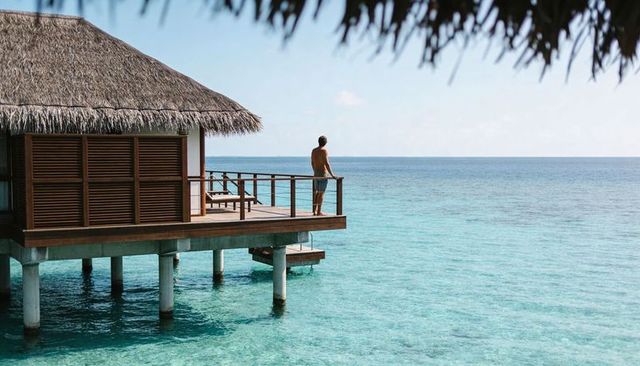 Man gazing over turquoise ocean from overwater bungalow deck at tropical resort