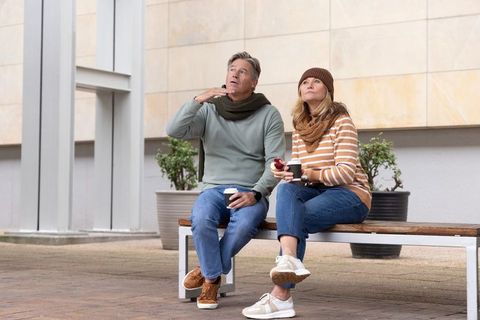 Senior couple enjoying coffee and snack on urban bench in cozy winterwear