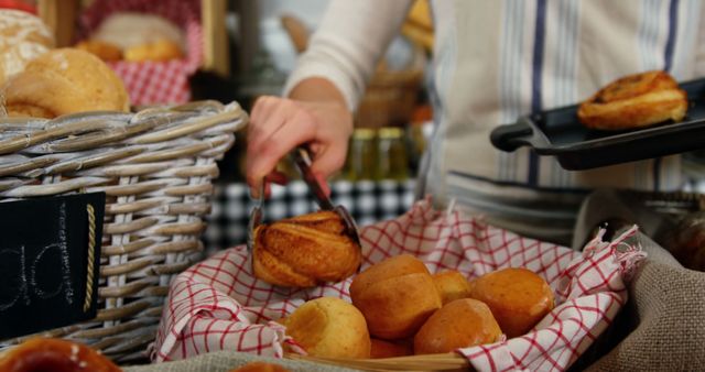 Person serving freshly baked buns from basket with other baked pastries on display. Ideal for use in articles or advertisements related to bakeries, morning breakfast options, homemade baking, and artisan food displays.