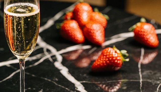 Fizzy champagne flute with ripe strawberries on black marble countertop