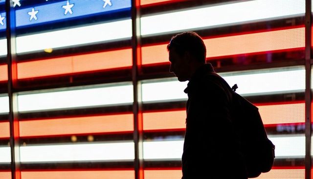 Silhouette walking commuter passing led american flag wall backlit with bold red stripes