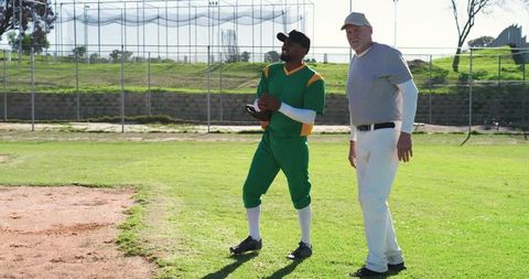 Senior coach mentoring diverse baseball player during sunny practice on community ballpark