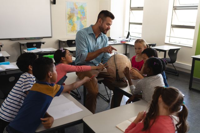 Male teacher engaging with diverse group of elementary school students using a globe to teach geography. Ideal for educational content, school brochures, teaching resources, and articles on interactive learning methods.