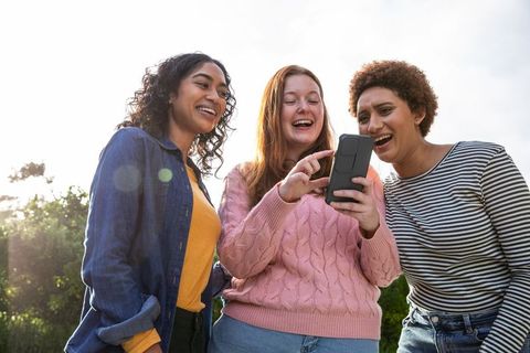 Diverse Female Friends Laughing at Smartphone Together Outdoors