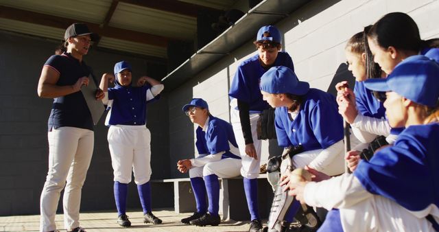 Diverse group of female baseball players and coach, coach instructing players on bench. female baseball team, sports training and game tactics.