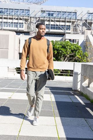 African American male walking with skateboard and headphones in urban plaza sunlight