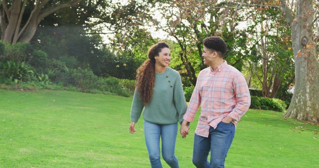 This image shows a happy couple enjoying a casual stroll in a lush green park while holding hands. Ideal for use in advertisements, brochures, or websites promoting romantic getaways, lifestyle blogs, relationship topics, health and well-being, or leisure activities.