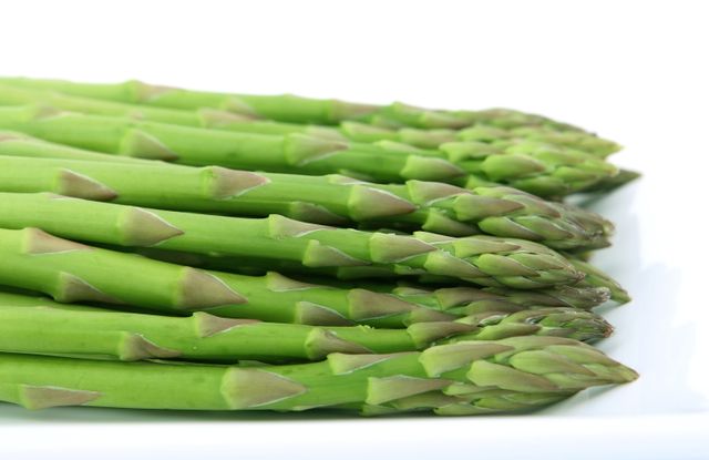 This image depicts fresh green asparagus spears arranged on a white background. Suitable for promoting healthy eating, organic food stores, or vegetarian recipes. Can be used in blogs, articles, and advertisements related to nutrition and farming.
