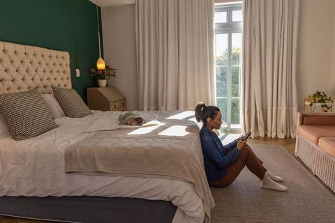 Sunlit bedroom solitude: young mother sitting on floor checking phone while newborn naps