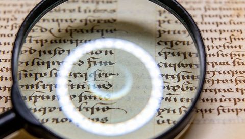Magnifying glass revealing antique manuscript calligraphy on vellum with light reflection