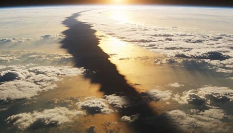 Dark cloud band splitting sunlit cloud tops over curved horizon at golden sunrise