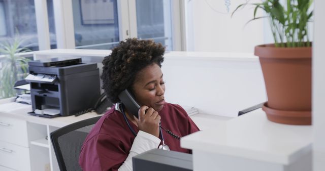 A medical receptionist dressed in a uniform is answering phone calls in a modern healthcare office. This scene is suitable for illustrating concepts related to healthcare administration, customer service in medical settings, professional work environments, and communication in the medical field.