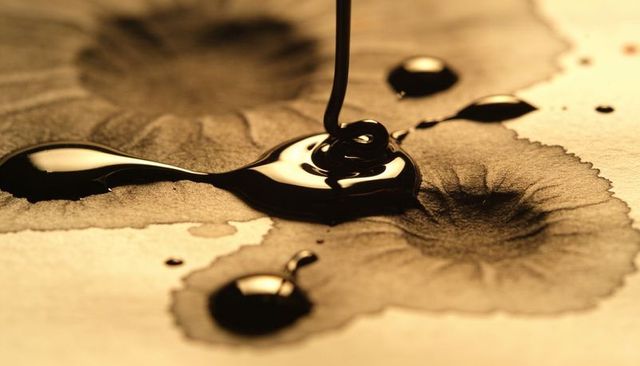 Pouring glossy black ink forming rippling halos on absorbent paper macro texture