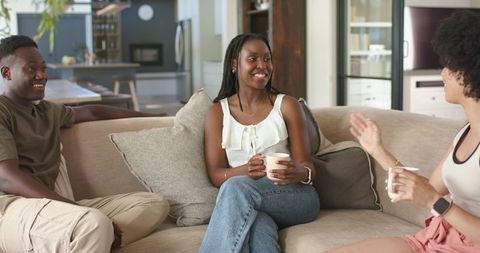 African American Friends Sitting on Sofa Sharing Coffee and Laughter in Modern Living Room