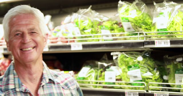 Senior man smiling while shopping for fresh vegetables in a supermarket. Ideal for content on healthy eating, retirement activities, active lifestyle for seniors, and grocery shopping habits.