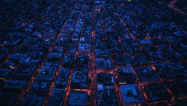 Aerial night grid of downtown with neon-lit streets and geometric rooftop patterns