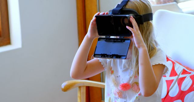 Young girl using VR headset in living room. Perfect for technology-themed articles, educational blogs highlighting new learning tools, or gaming websites illustrating VR in daily life.