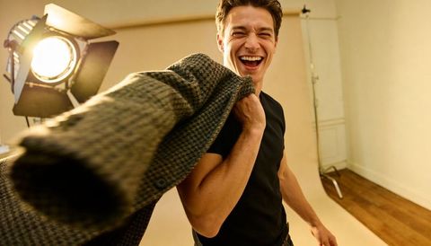 Laughing male model holding tweed jacket over shoulder under warm barn-door studio light