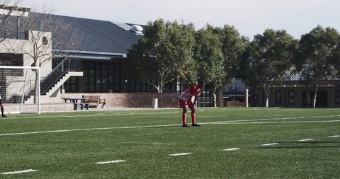 Youth soccer player in red uniform on field near school buildings