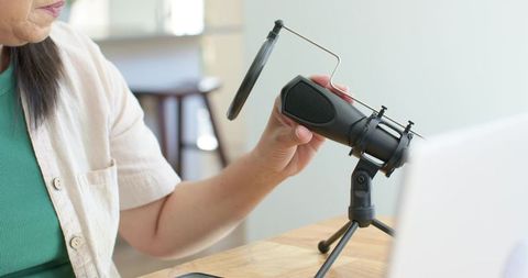Mature asian woman adjusting condenser microphone for home podcasting and remote recording