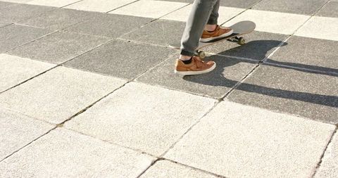 Adult male balancing on skateboard on checkerboard urban plaza tiles in brown sneakers