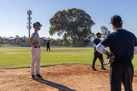 Baseball players on neighborhood diamond standing on base watching pitcher during casual game