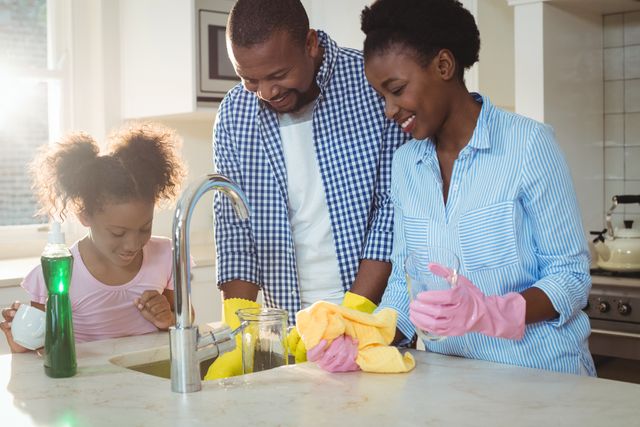 African American family washing dishes in kitchen. Parents and daughter smiling and working together. Great for themes of family bonding, domestic life, home chores, and teamwork.
